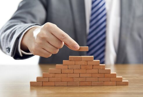 Businessman in a suit putting the last piece of a pyramid using wooden blocks